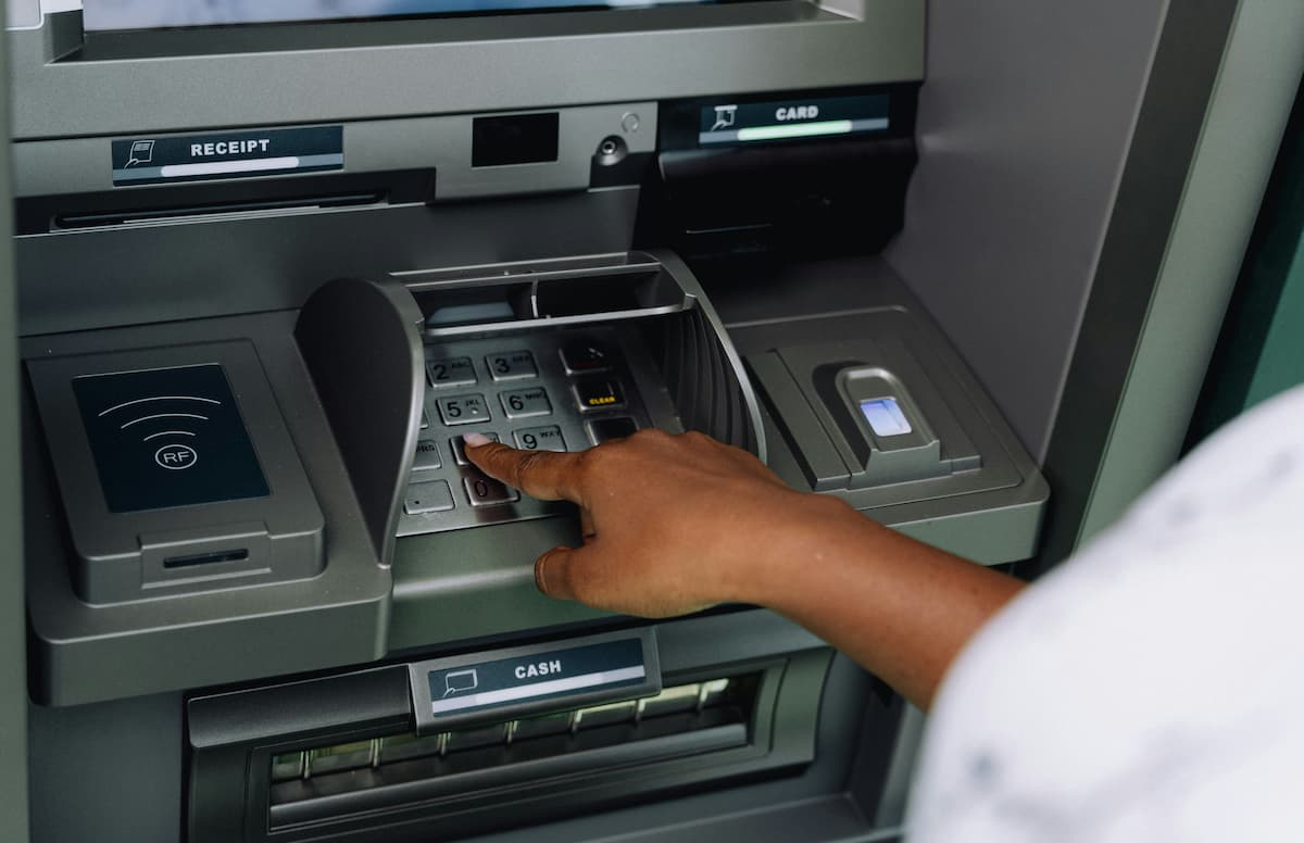 Close-up of a person's hand entering a PIN on the keypad of an ATM.